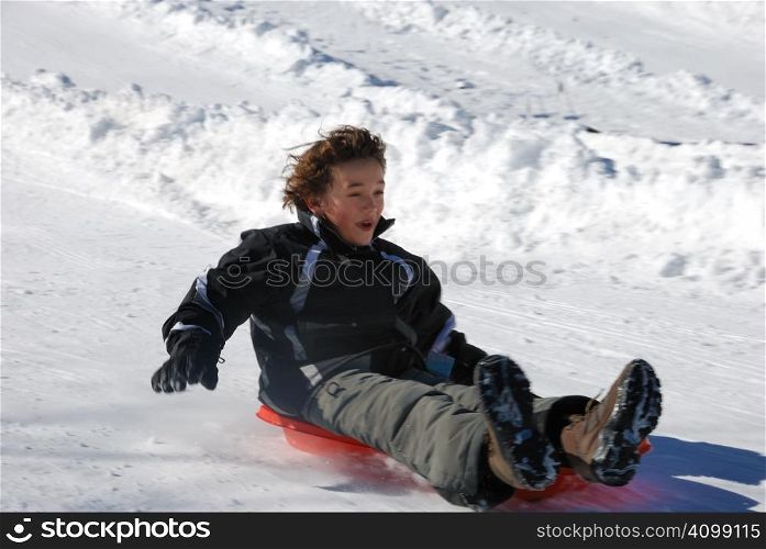 boy sledding fast down the hill on a red sled with snow background