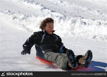 boy sledding fast down the hill on a red sled with snow background