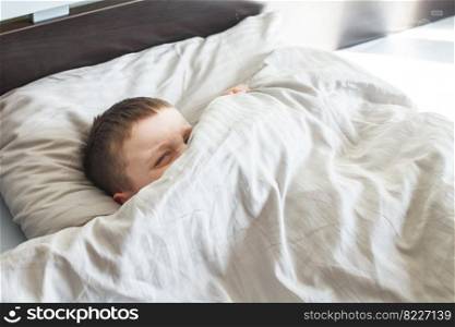 boy sleep in the bed. the child lies on a pillow and covers his face with a blanket. boy sleep in the bed. child lies on pillow and covers his face with a blanket