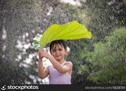 Boy smiling, having fun, stands with leaf on her head standing in the rain.