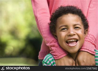 Boy smiling with mother standing behind him with hands on shoulders.
