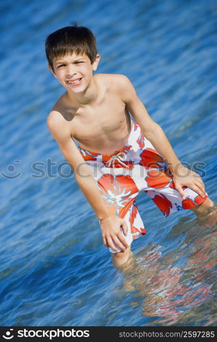 Boy standing in water with his hands on his knees