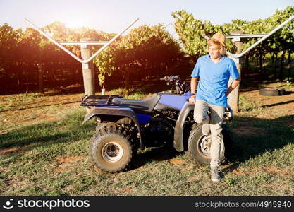 Boy standing next to truck in vineyard. Boy wearing hat standing next to truck in vineyard