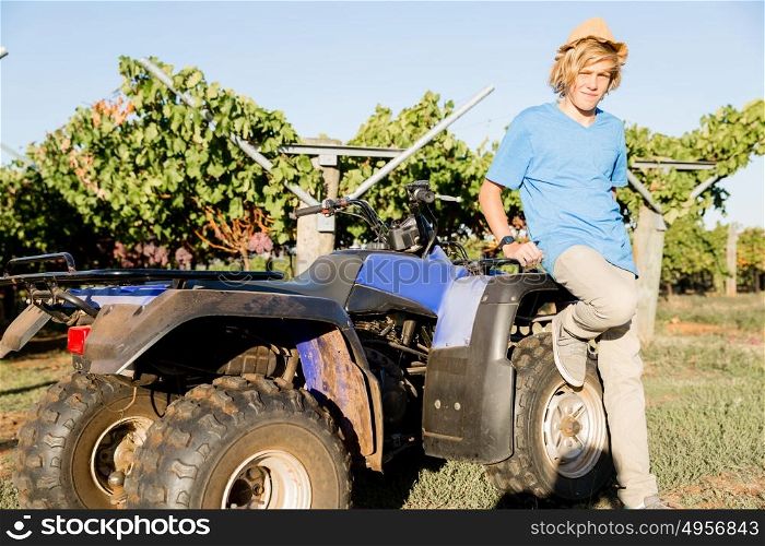 Boy standing next to truck in vineyard. Boy wearing hat standing next to truck in vineyard