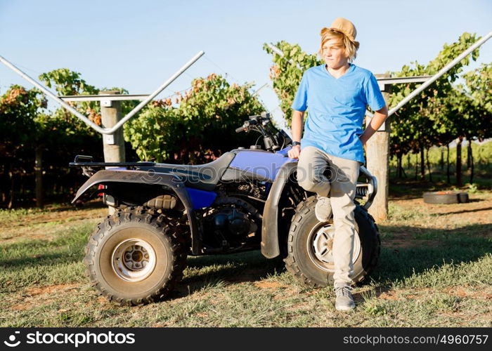 Boy standing next to truck in vineyard. Boy wearing hat standing next to truck in vineyard