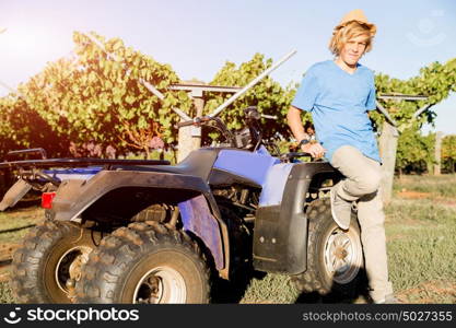 Boy standing next to truck in vineyard. Boy wearing hat standing next to truck in vineyard