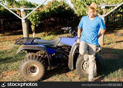 Boy standing next to truck in vineyard. Boy wearing hat standing next to truck in vineyard