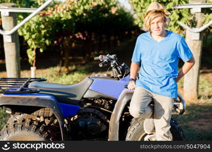 Boy standing next to truck in vineyard. Boy wearing hat standing next to truck in vineyard