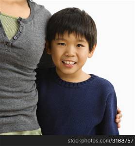 Boy standing smiling with mother standing next to him with arm around him.