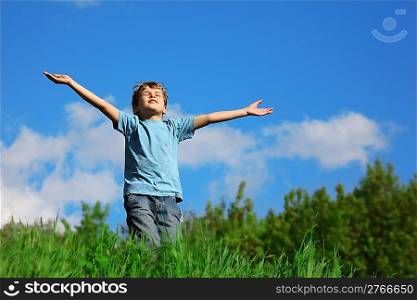 boy standing with spreading hands on the field against the sky