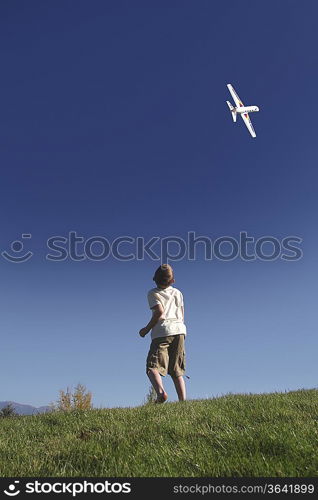 Boy stands on hilltop flying model plane