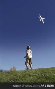 Boy stands on hilltop flying model plane