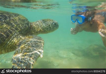 Boy swimming with a giant sea turtle in the ocean in Sri Lanka
