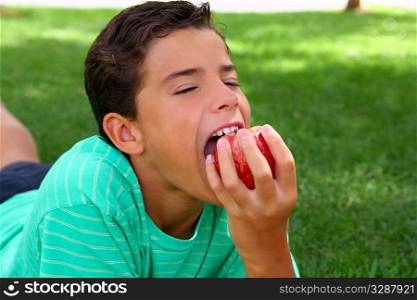 boy teenager eating red apple laying on garden grass outdoors