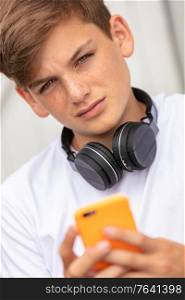 Boy teenager teen male child outside using his mobile cell phone and bluetooth wireless headphones for social media