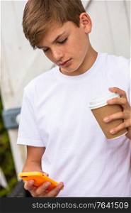 Boy teenager teen male child outside using his mobile cell phone and drinking takeout tea or coffee