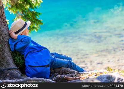 Boy tired traveler with a backpack resting at a lake in the Tatr. Boy tired traveler with a backpack resting at a lake in the Tatra Mountains