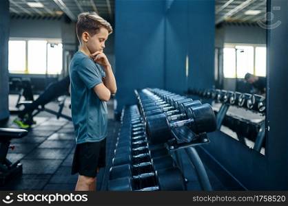 Boy tries to take heavy dumbbell in gym. Youngster on training in sport club, healthcare and healthy lifestyle, schoolboy on workout. Boy tries to take heavy dumbbell in gym