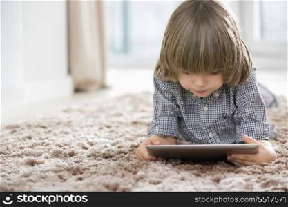 Boy using digital tablet while lying on rug at home