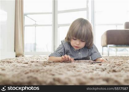 Boy using digital tablet while lying on rug in living room