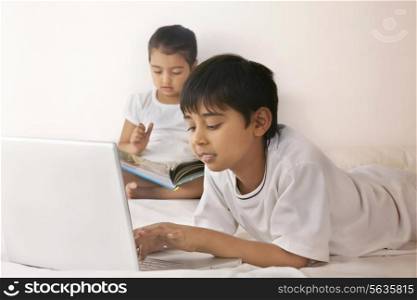 Boy using laptop while girl reading book in bed
