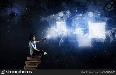 Boy using modern technologies. Cute school boy sitting on pile of books and using his smartphone