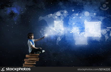 Boy using modern technologies. Cute school boy sitting on pile of books and using his smartphone