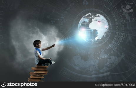 Boy using modern technologies. Cute school boy sitting on pile of books and using his smartphone