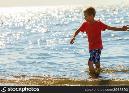 Boy walking on beach.. Water fun and joy outside. Little boy walking through the sea ocean. Lonely kid playing outdoors in summer clothes.