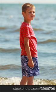 Boy walking on beach.. Water fun and joy outside. Little boy walking through the sea ocean. Lonely kid playing outdoors in summer clothes.
