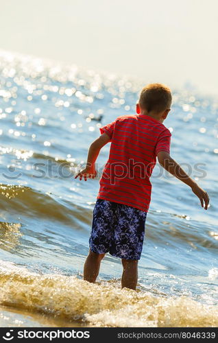 Boy walking on beach.. Water fun and joy outside. Little boy walking through the sea ocean. Lonely kid playing outdoors in summer clothes.
