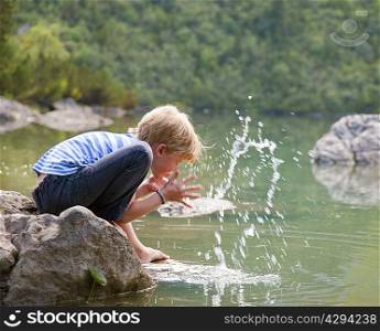 Boy washing his face in still lake