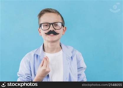 boy wearing black eyeglasses holding black moustache prop front his upper lips