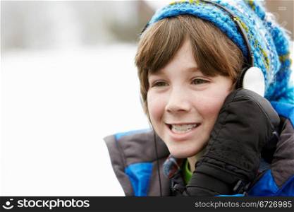 Boy Wearing Headphones And Listening To Music Wearing Winter Clothes In Snowy Landscape