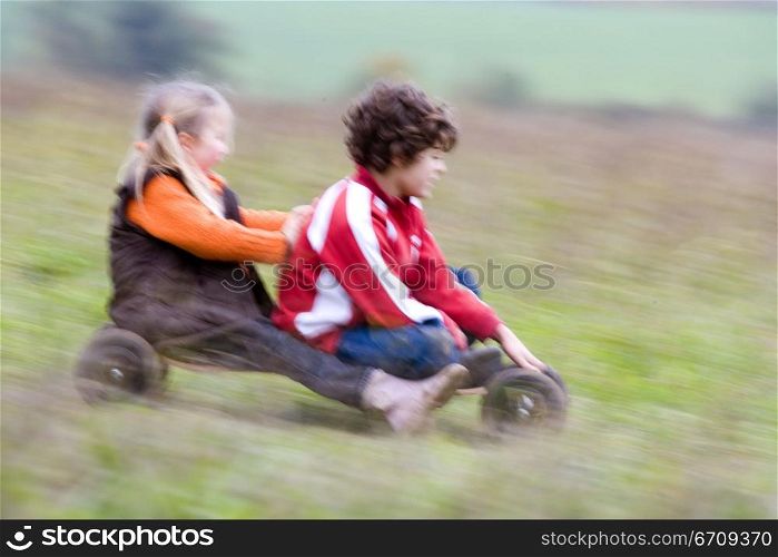 Boy with a girl riding a mountain board in a field