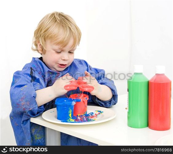 Boy with an apron playing with various colors finger paint