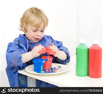 Boy with an apron playing with various colors finger paint
