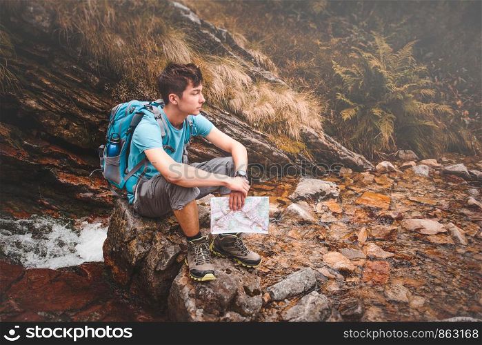 Boy with backpack sitting on a rock on during a trip in mountains