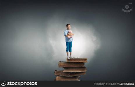 Boy with bear toy. Cute little boy with toy bear standing on pile of books