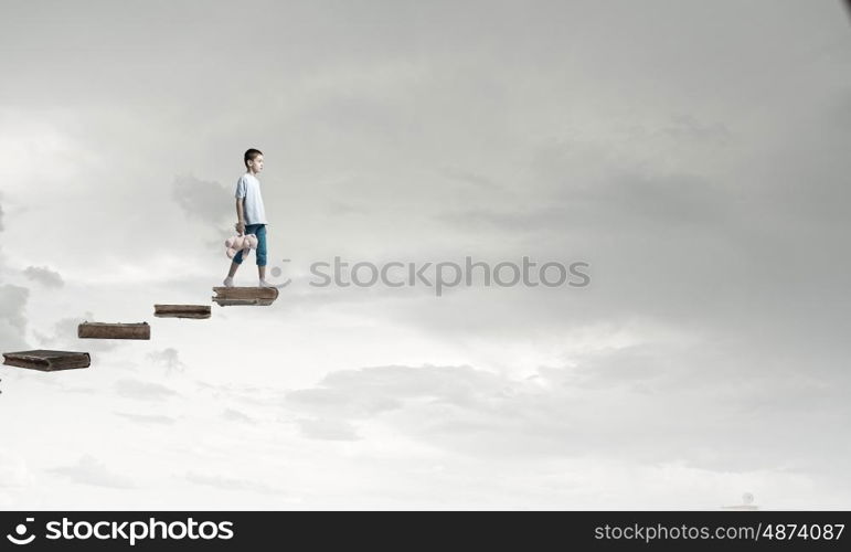 Boy with bear toy. Cute little boy with toy bear walking on ladder of books