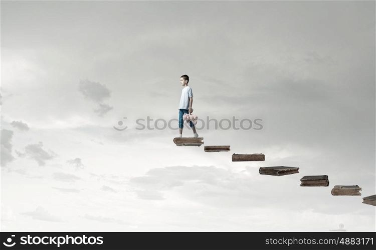 Boy with bear toy. Cute little boy with toy bear walking on ladder of books