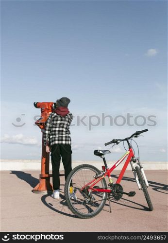 boy with bicycle looking through telescope outdoors