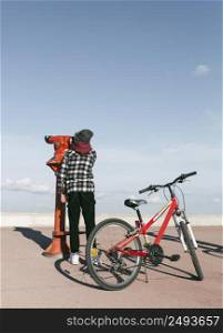 boy with bicycle looking through telescope outdoors