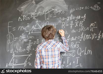Boy with chalk writting on math formulas black board. Boy writting on black board