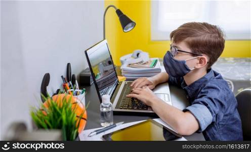 Boy with face mask doing homework with laptop in his bedroom