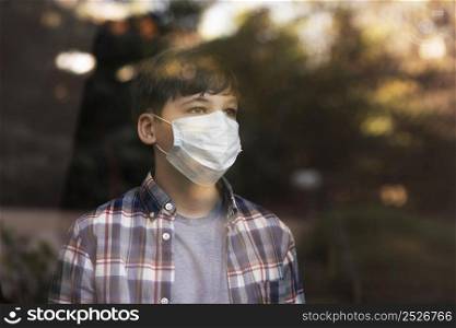 boy with face mask looking outdoors through windows