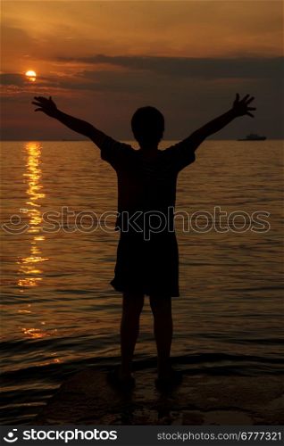 boy with his hands raised in the sunset over the sea