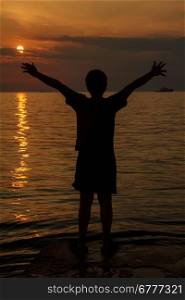 boy with his hands raised in the sunset over the sea