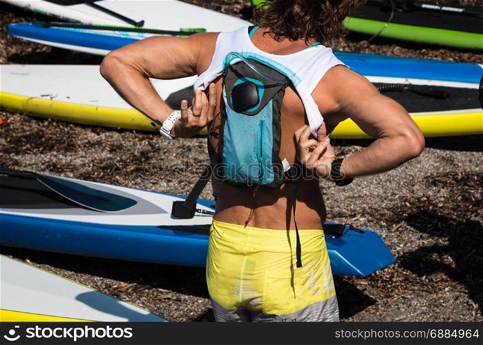 Boy with Hydration Pack on His Shoulder Wearing White Shirt before Surfing, Stand Up Paddle Boards in Background