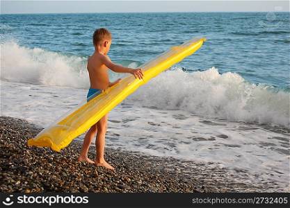 boy with inflatable mattress stands on seacoast